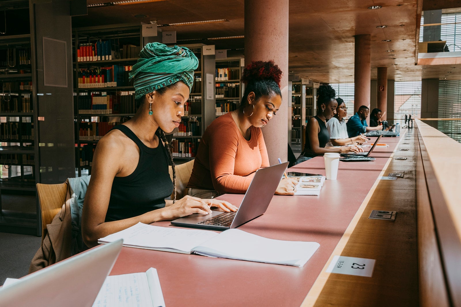 Woman wearing turban using laptop while sitting with friend in library