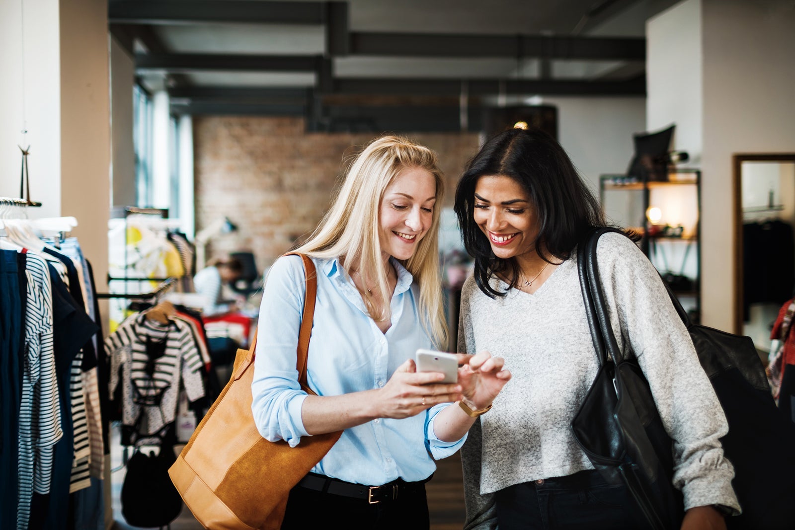 Two Womem Looking At Smartphone While Clothes Shopping