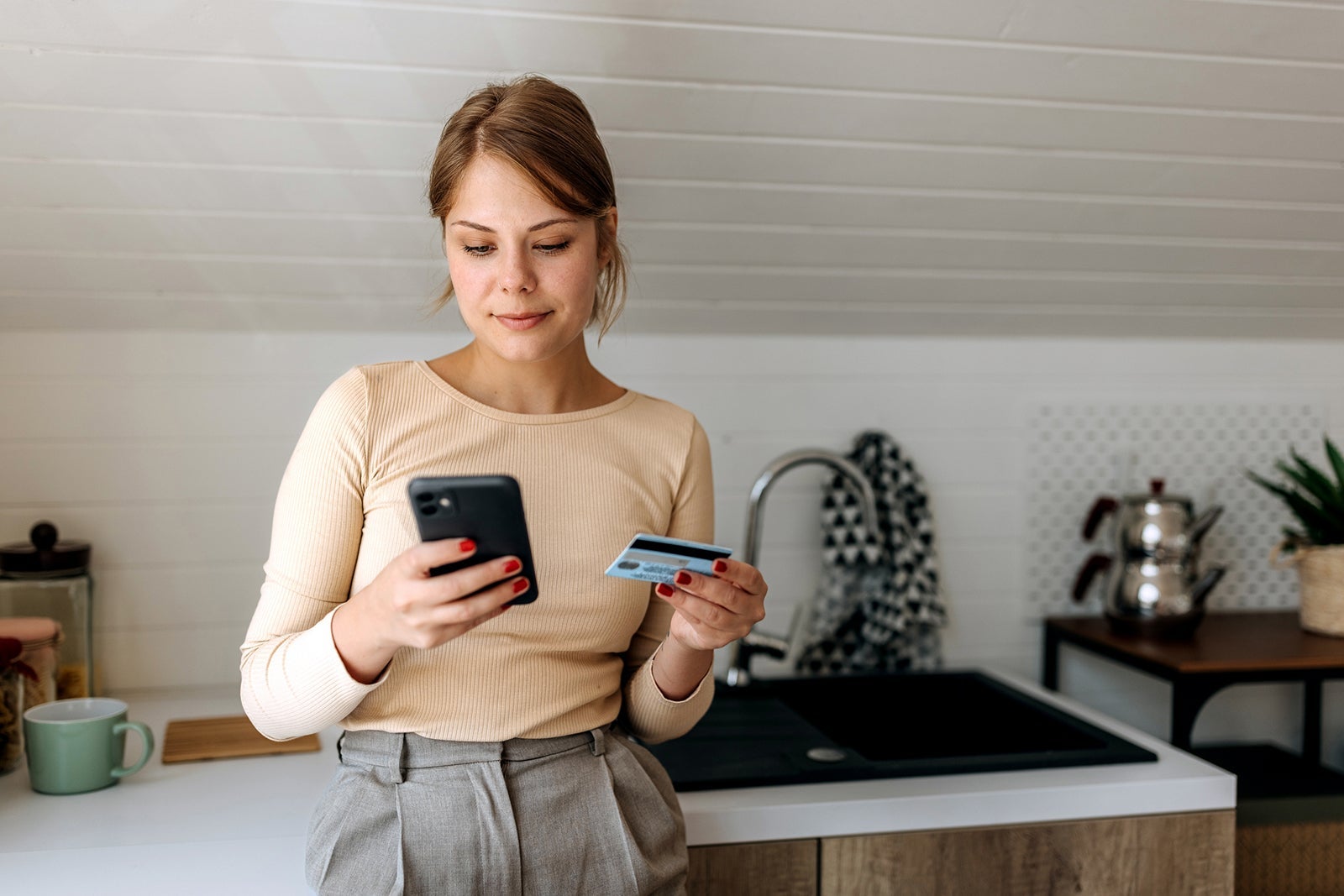 Young casually clothed woman online shopping from her domestic kitchen