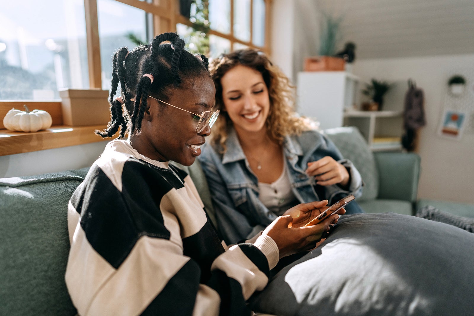 Two young casually clothed female students using phone at home